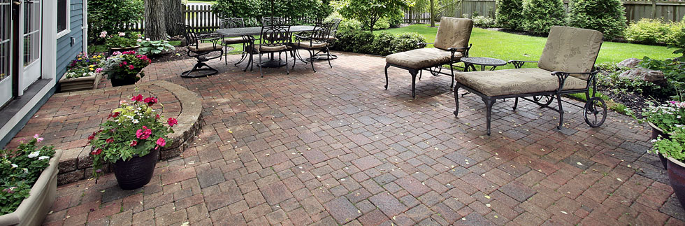 Outdoor dining furniture and two loungers on a large patio edged with bushes and plants in tubs