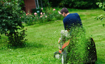 A man riding a motor mower across a lawn, with grass flying up behind him
