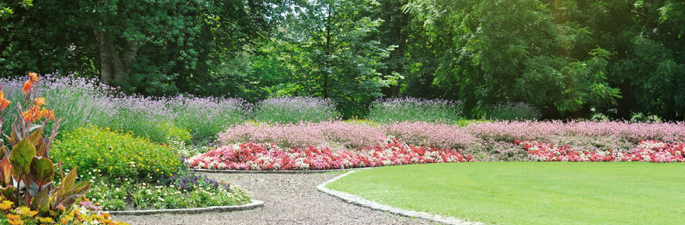 Beds of colourful flowers around a green lawn edged with shale paving